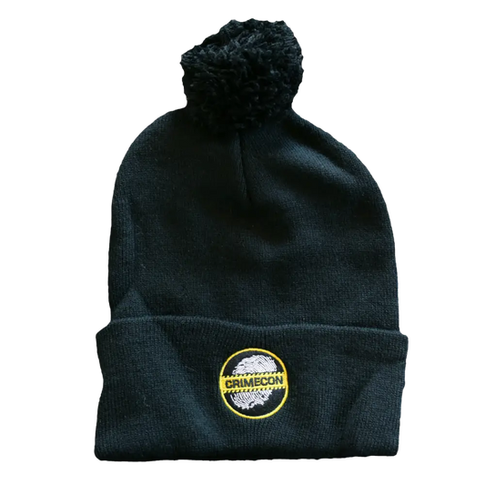 Black knit beanie with a pom-pom and circular logo patch.