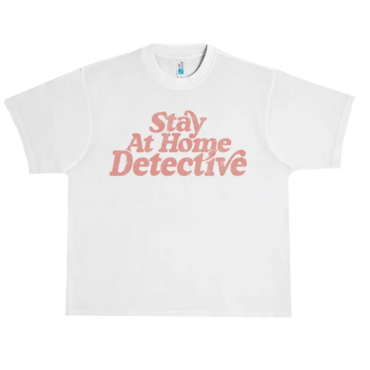 White t-shirt with pink text reading ’Stay At Home Detective’.